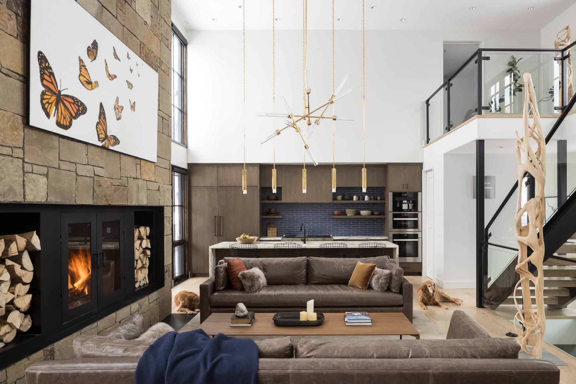 Modern living room with stone fireplace, brown sofas, and open kitchen in a bright double-height space