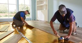 Two workers installing a wooden floor in a bright room