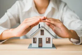 Hands protecting a small house model on a table