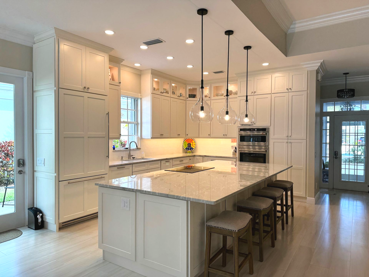 Bright white kitchen with island, pendant lights, built-in ovens, and barstools under glossy floors.