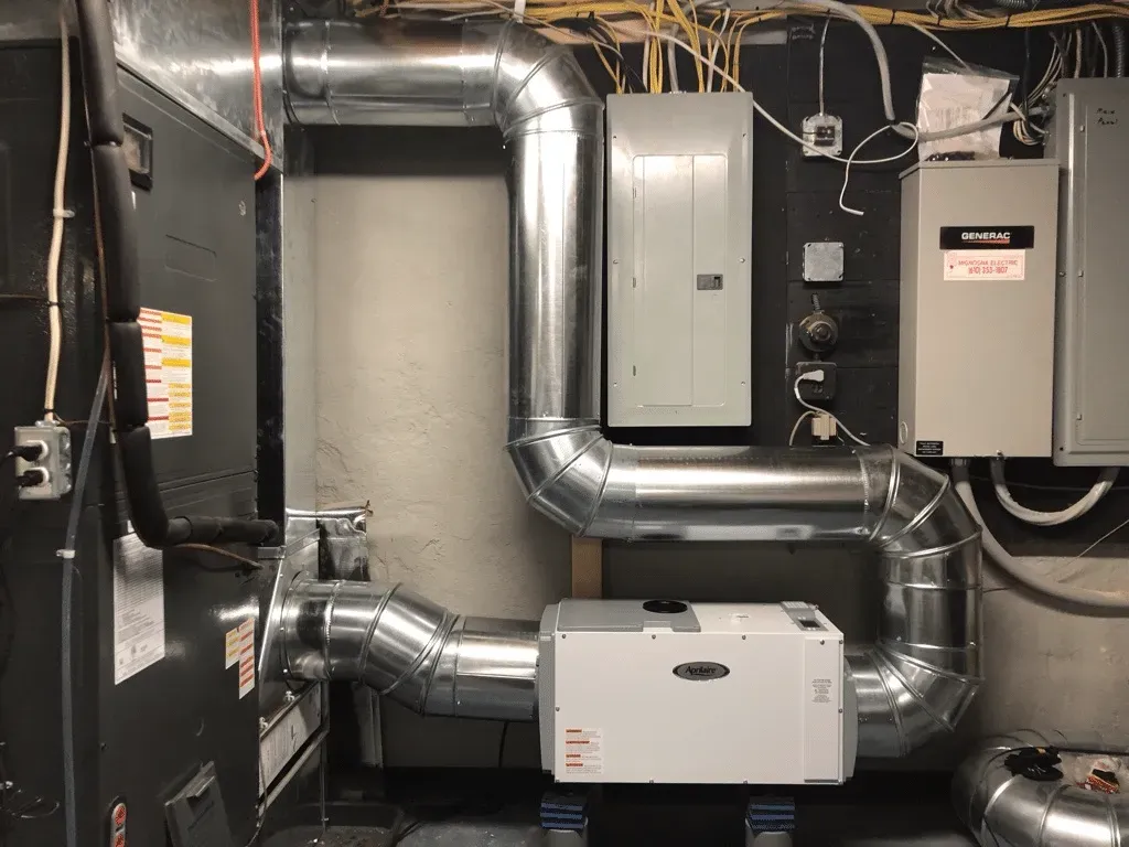 Basement utility room with silver HVAC ducts, electrical panels, and equipment mounted on the wall