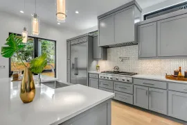 Modern gray kitchen with white island, stainless stove, pendant lights, and vase of flowers near large windows