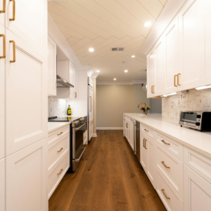 Bright, narrow galley kitchen with white cabinets, wood floor, and stainless steel appliances
