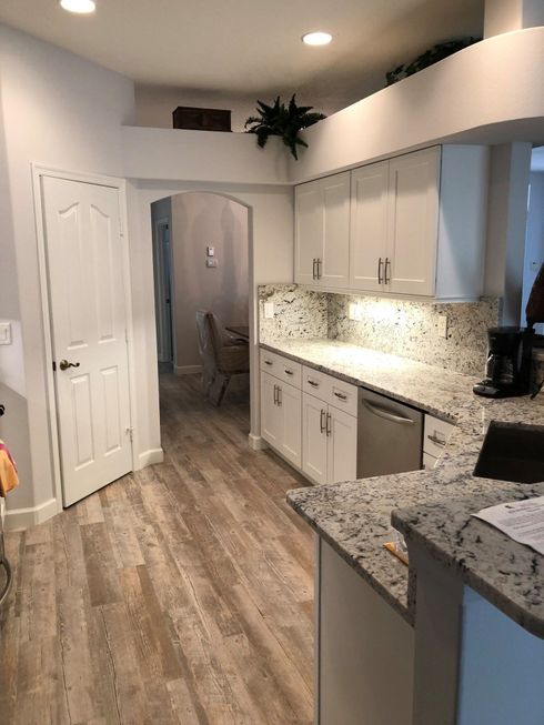 Bright kitchen with white cabinets, granite counters, wood-look floor, and recessed lighting.