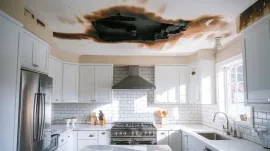 Modern white kitchen with a large ceiling leak and water-damaged, collapsed drywall above the stove