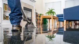 Vacuum cleaning a shiny living room floor near blue chairs and a wooden table