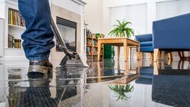 Vacuum cleaning a shiny living room floor near blue chairs and a wooden table