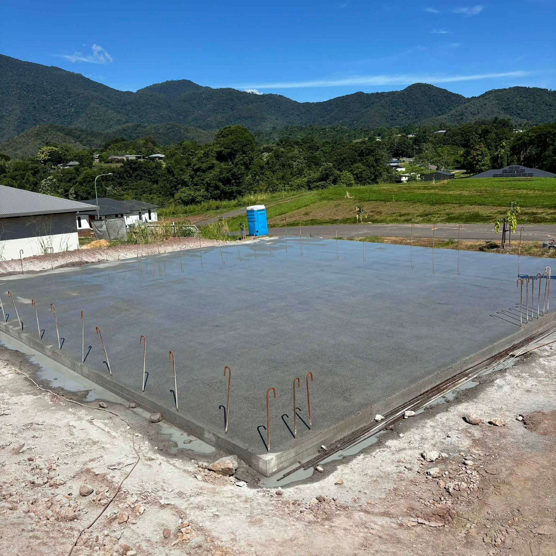 A construction worker in blue work pants and boots pours wet concrete from a hose onto a wire mesh frame at a site.