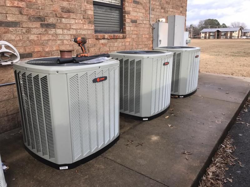 Three outdoor air conditioning units next to a brick building.