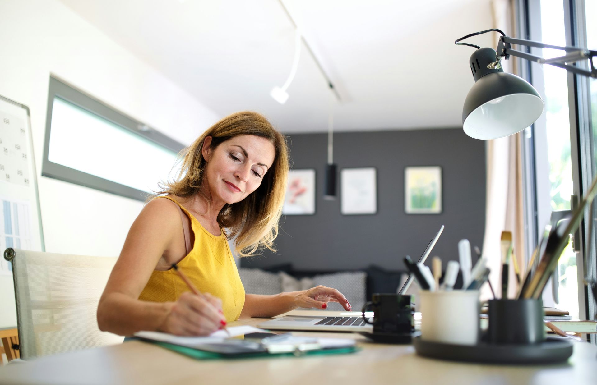 Woman in yellow top writing at a desk in a bright home office