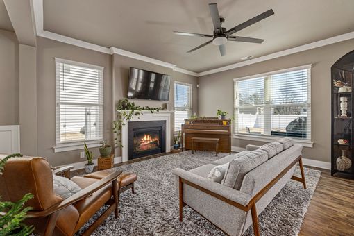 Bright living room with fireplace, sofa, leather chair, large windows, and ceiling fan