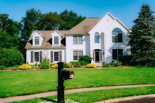 Large white suburban house with a green lawn and black mailbox in the foreground