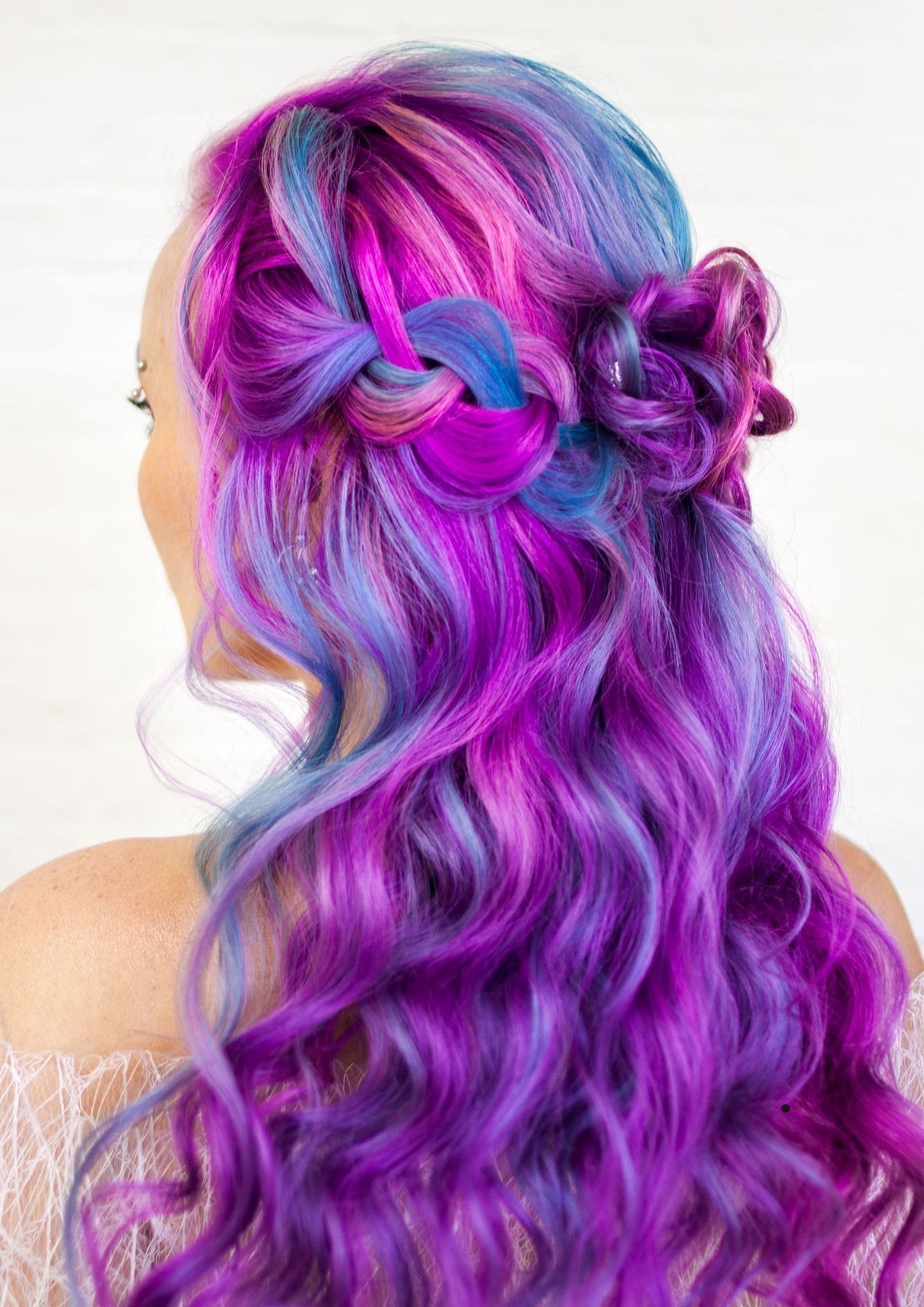 A woman with purple and blue hair is wearing headphones in her hair.