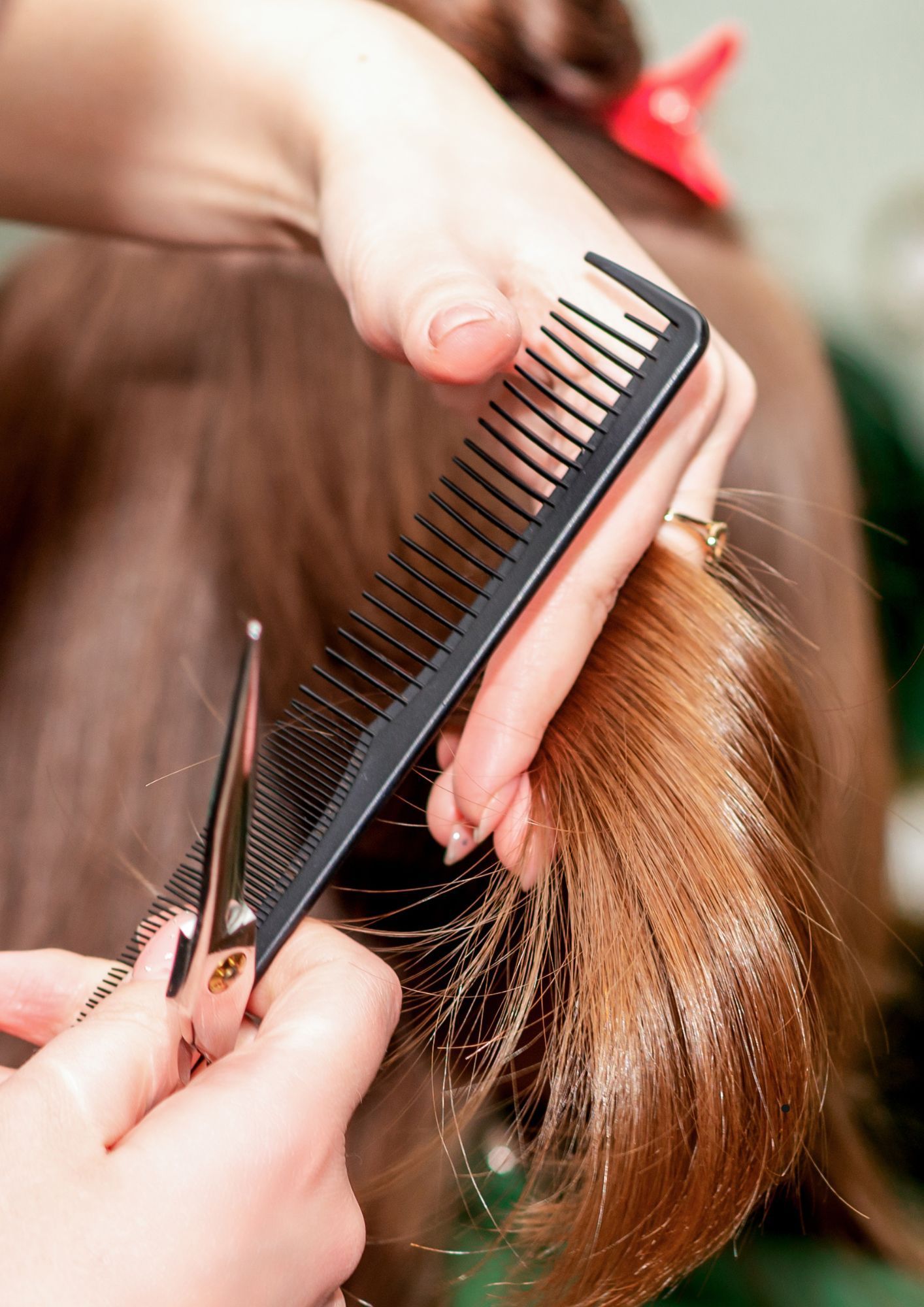 A woman is getting her hair cut by a hairdresser with scissors and a comb.