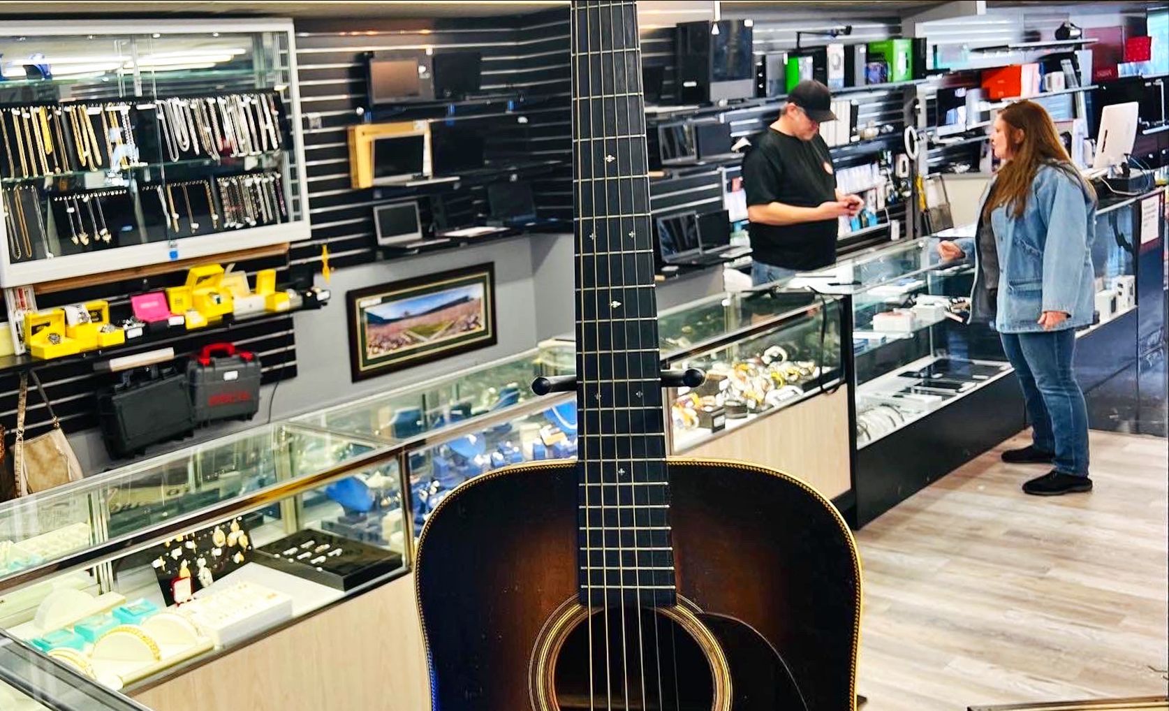 Acoustic guitar in a pawn shop; a customer and clerk are visible.