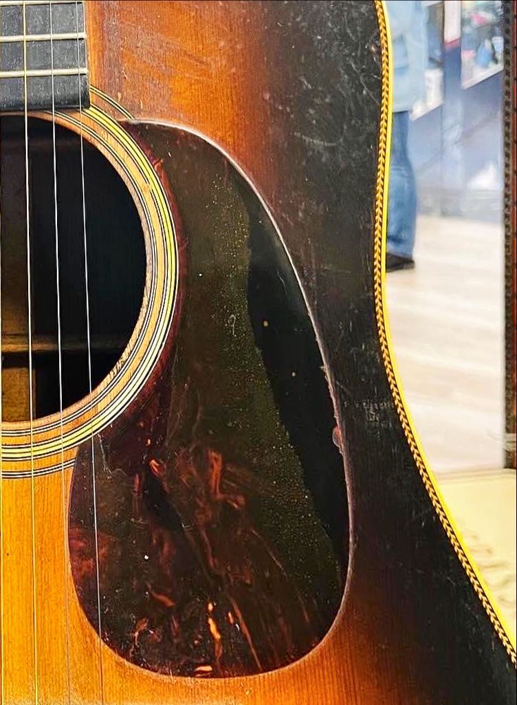 Close-up of an acoustic guitar, showing the soundhole, tortoiseshell pickguard, and weathered wood.