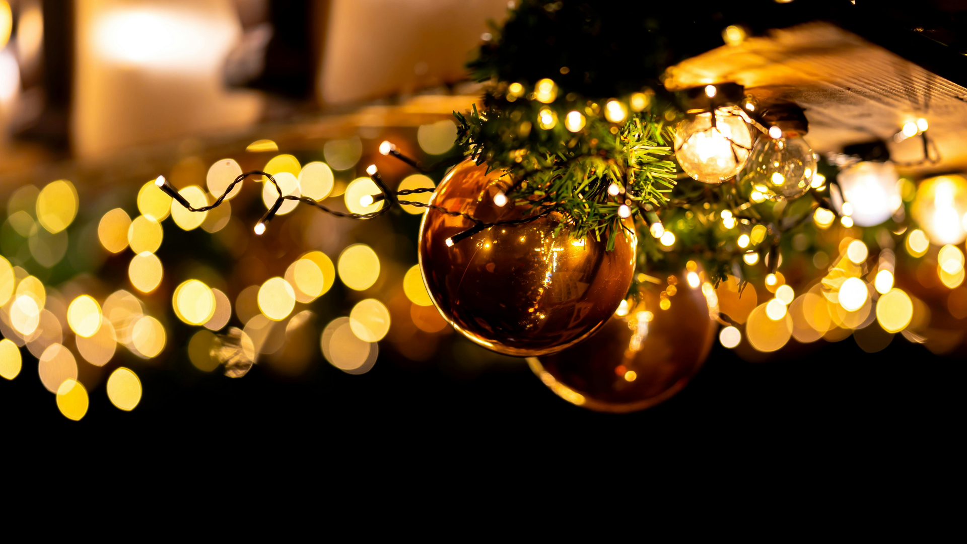 Christmas-decorated porch with small trees, glowing lights, wreath, and lanterns framing a weathered wooden door.