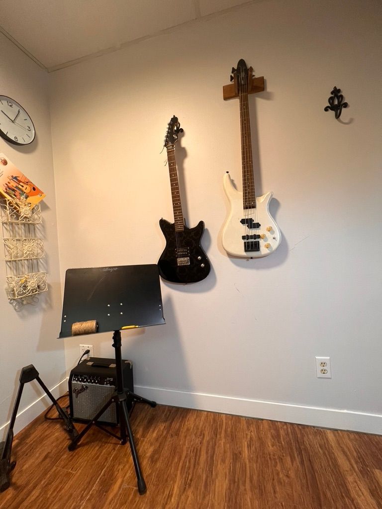 Two guitars are hanging on a wall next to a music stand.