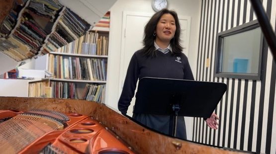 A woman is standing in front of a piano in a room.