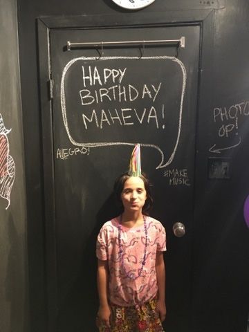 A little girl is standing in front of a door that says happy birthday maheva