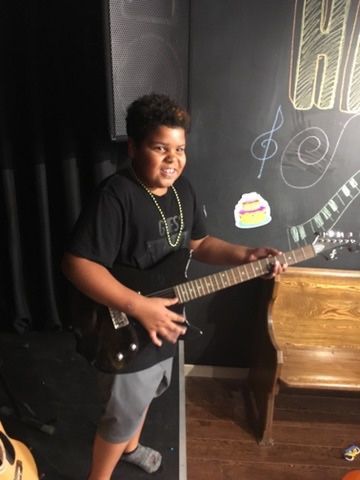 A young boy is holding a guitar in front of a chalkboard.