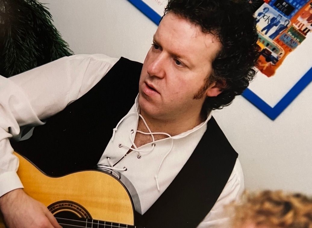A man in a white shirt and black vest is playing a guitar