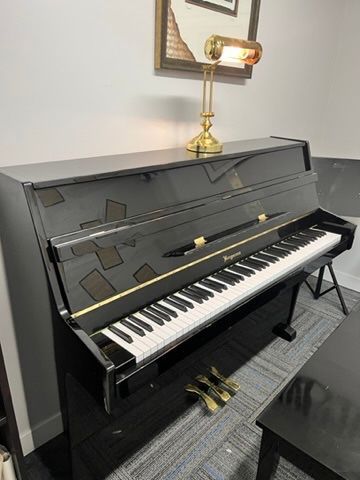 A black upright piano is sitting in a room next to a lamp.
