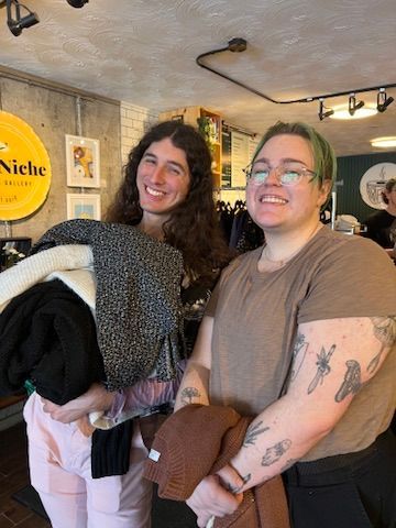 Two women are standing next to each other in a store holding clothes.