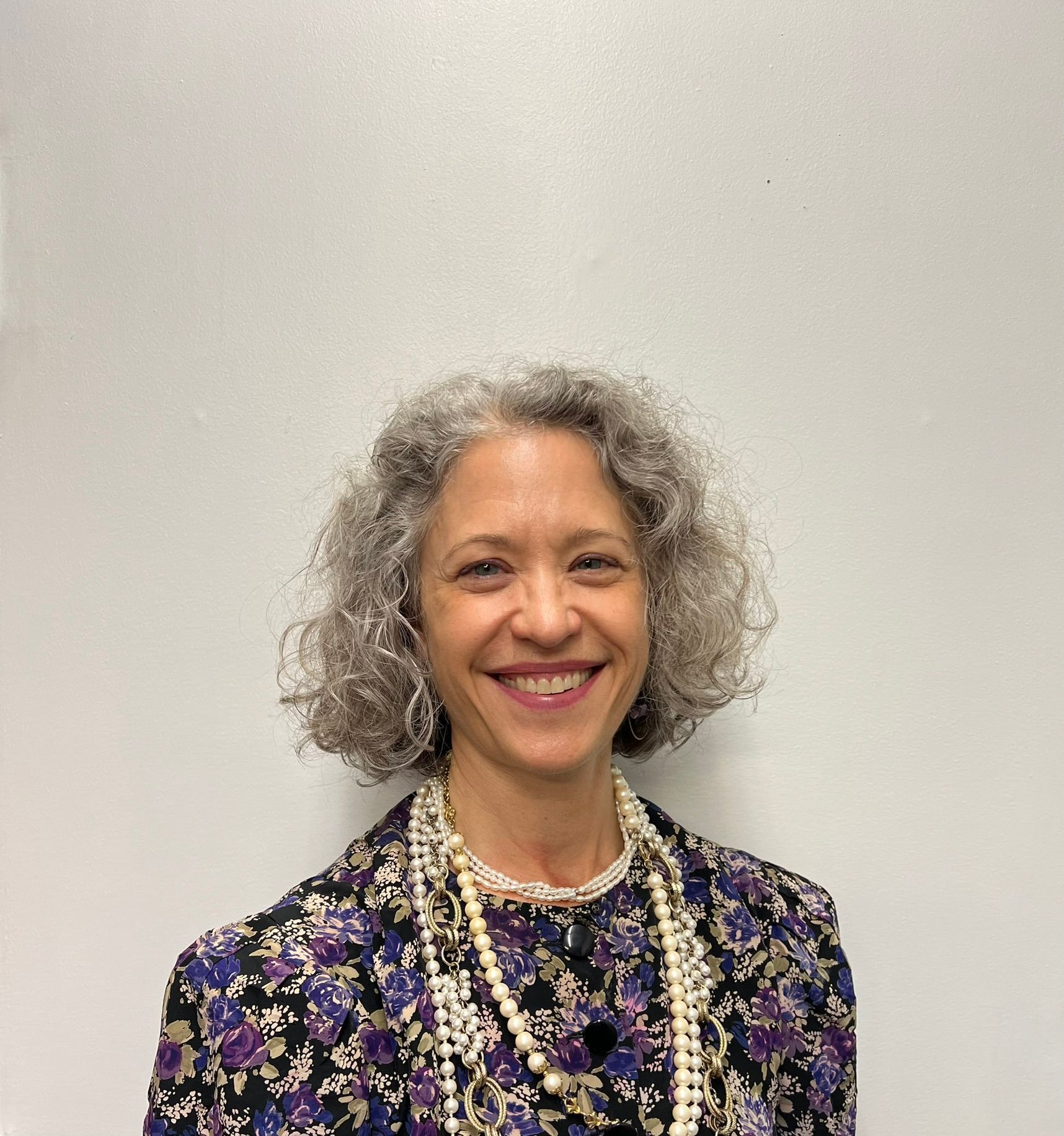 A woman with gray hair and a pearl necklace is smiling for the camera.