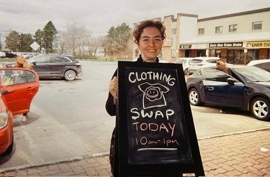 A woman is holding a sign that says clothing swap today