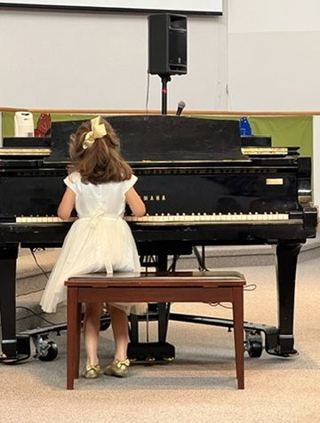 A little girl in a white dress is playing a piano