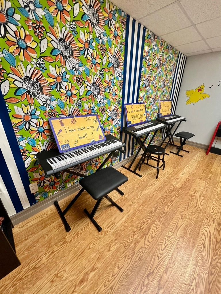 A room with a lot of keyboards and a floral wallpaper on the wall.