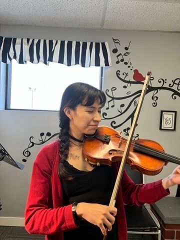 A woman is playing a violin in front of a window.