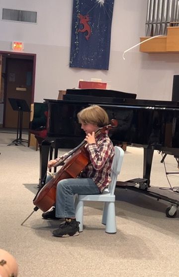 A young boy sits in a chair playing a cello