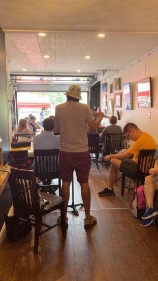 A man in a hat is standing in a restaurant with people sitting at tables.