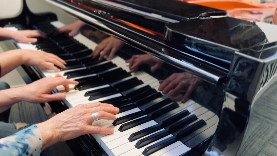 Two people are playing a piano with their hands on the keys.