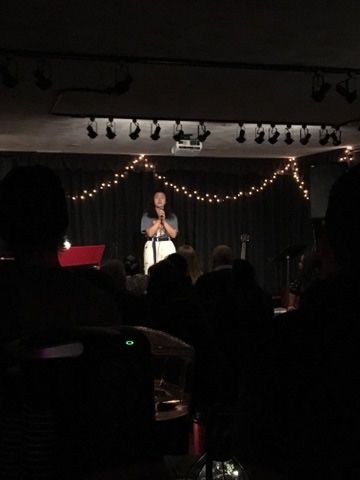 A woman is standing on a stage holding a microphone in front of a crowd.
