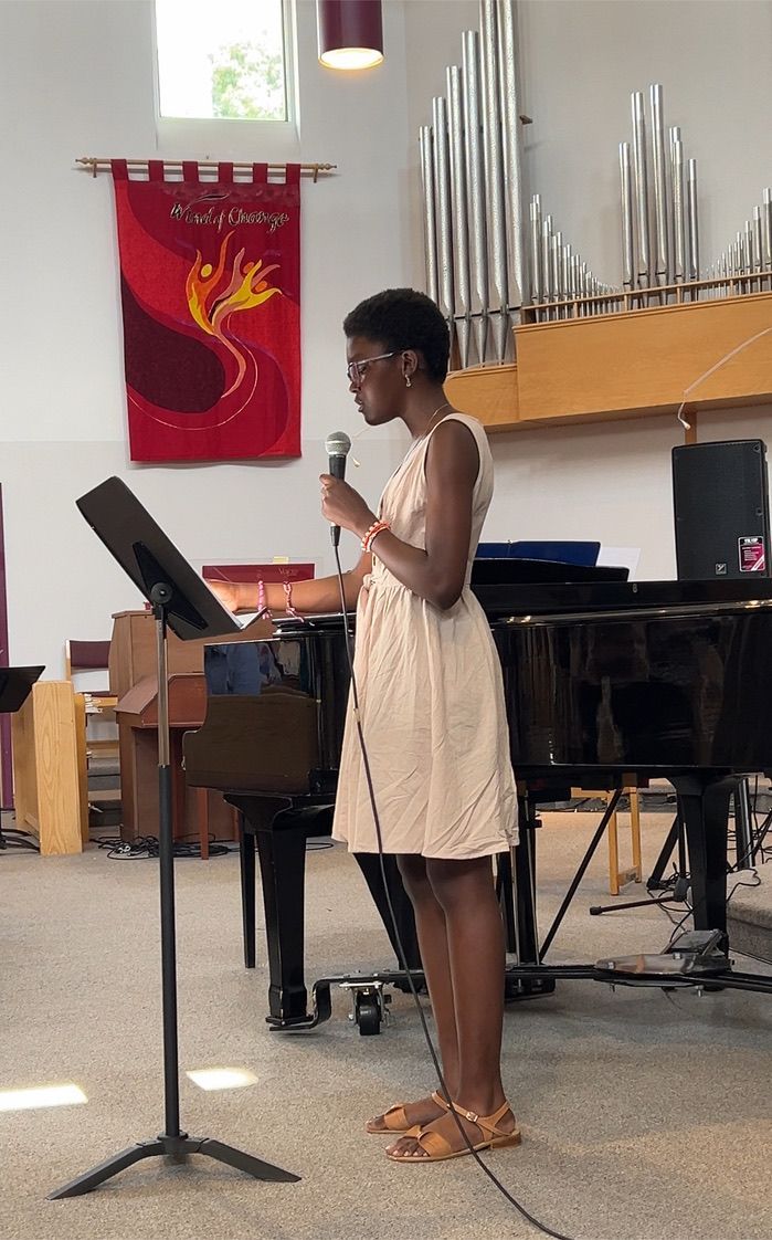 A woman is singing into a microphone in front of a piano in a church.