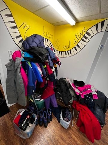 A bunch of clothes are hanging on a rack in a room with a piano keyboard mural on the wall.