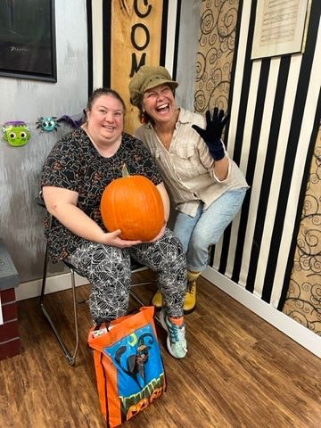 Two women are sitting next to each other holding pumpkins.