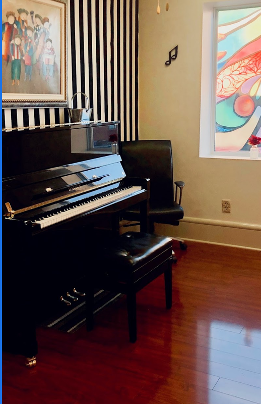Black upright piano with bench in a room with framed art and wood floor