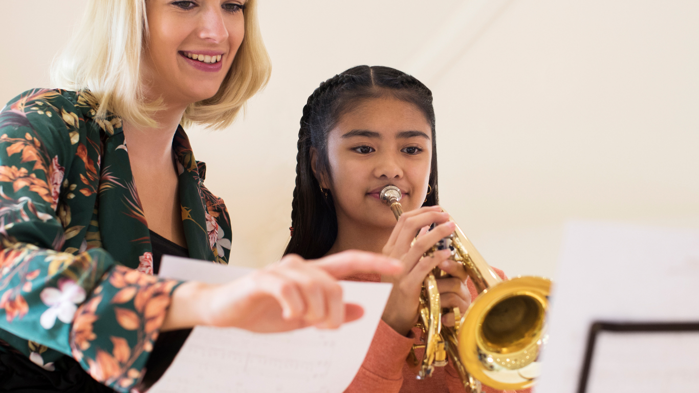 Teacher guiding a student playing trumpet during a music lesson