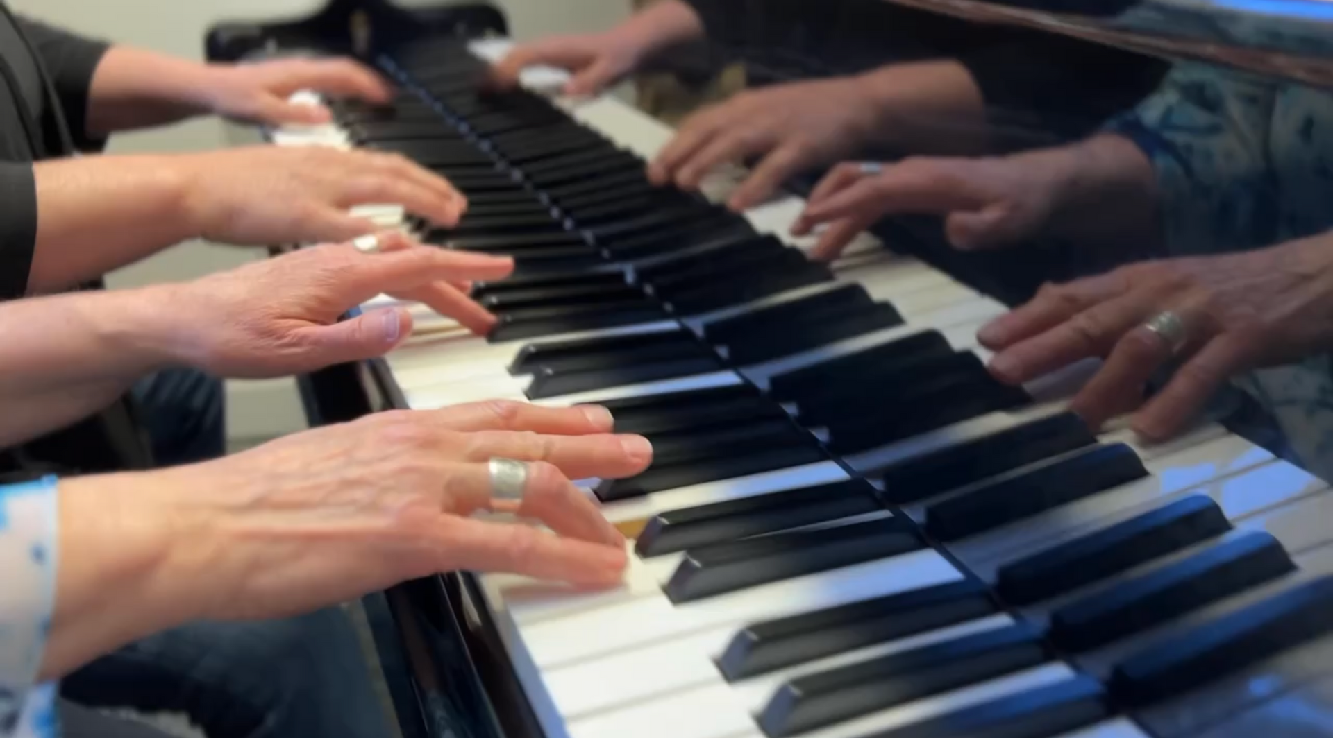 Hands playing a piano keyboard in a close-up view, with multiple reflections visible above the keys