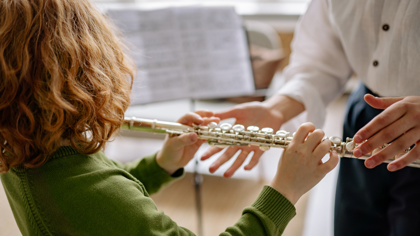 Person playing a silver flute while another person holds sheet music nearby