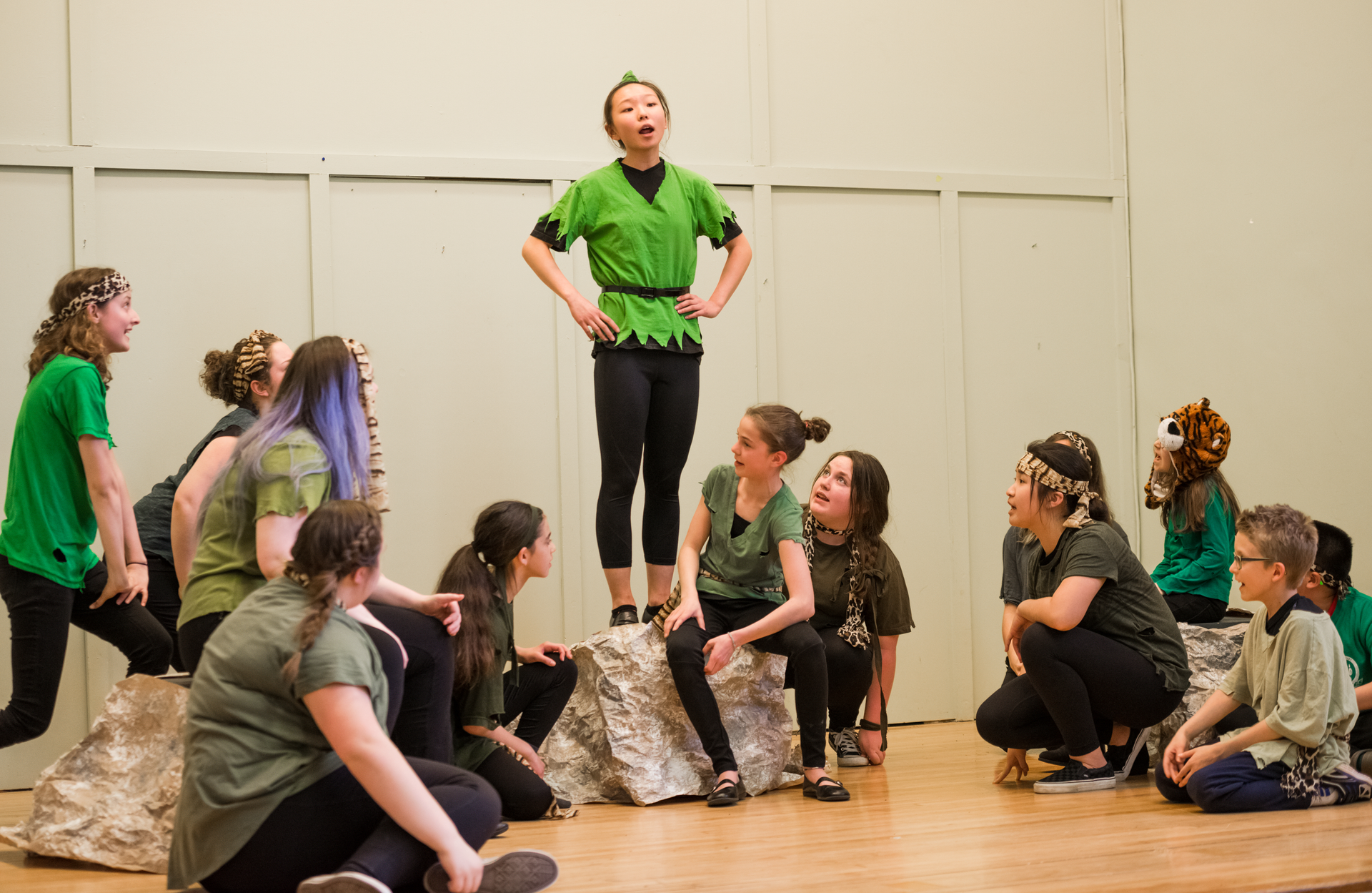 Group of performers in green shirts and costumes rehearsing on a stage