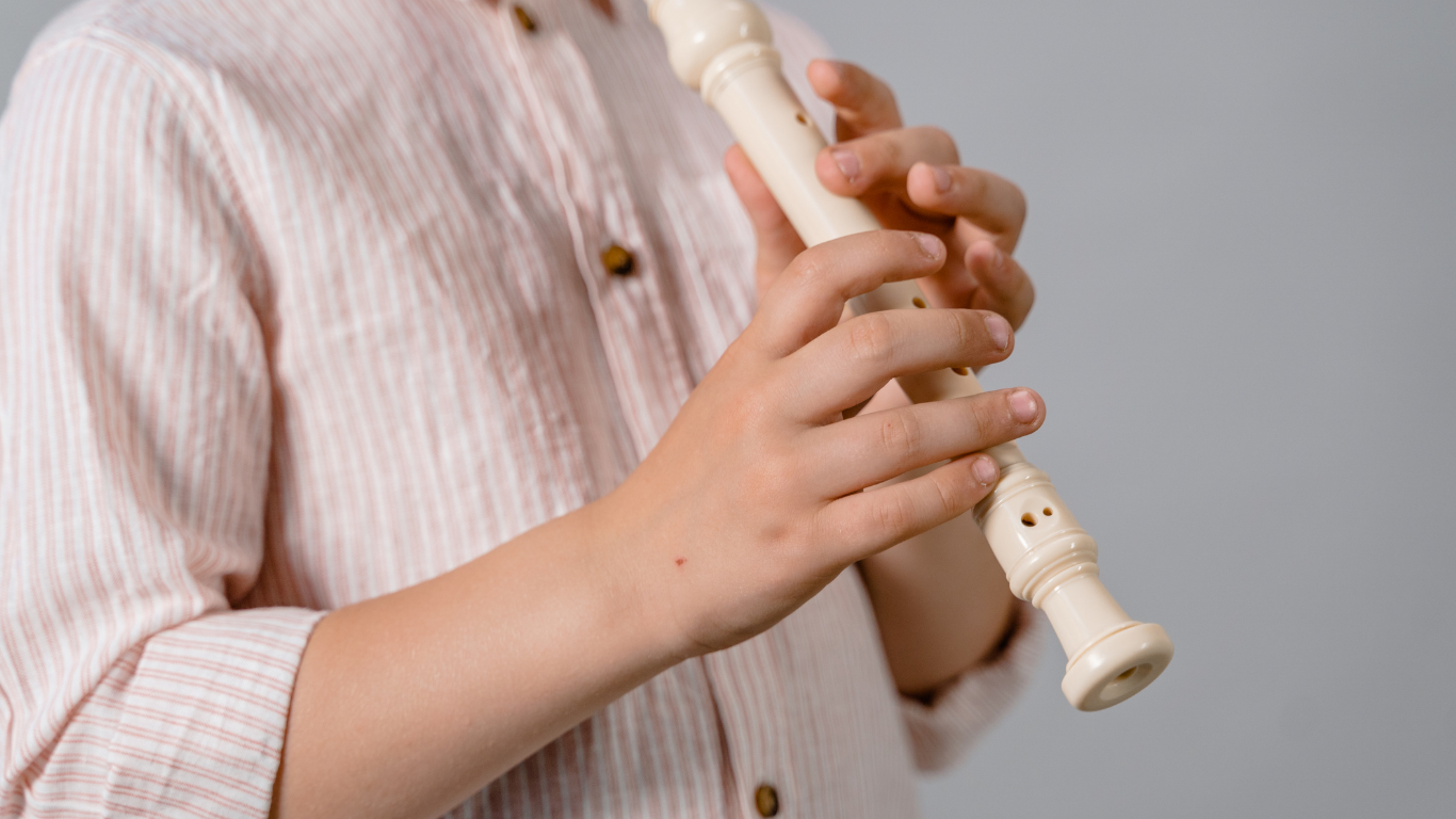 Hands holding and playing a white recorder against a light background