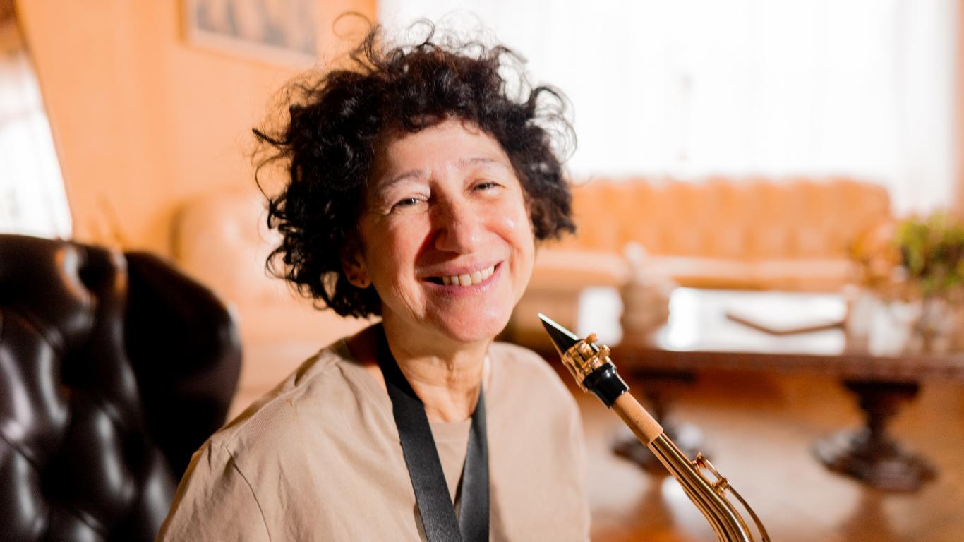 Smiling person holding a saxophone in a cozy, warmly lit room
