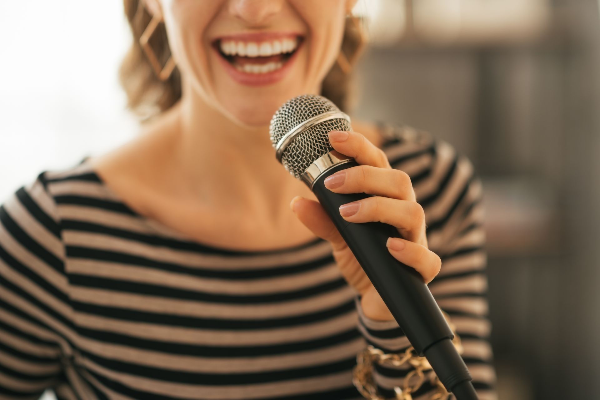 A woman in a striped shirt is singing into a microphone.