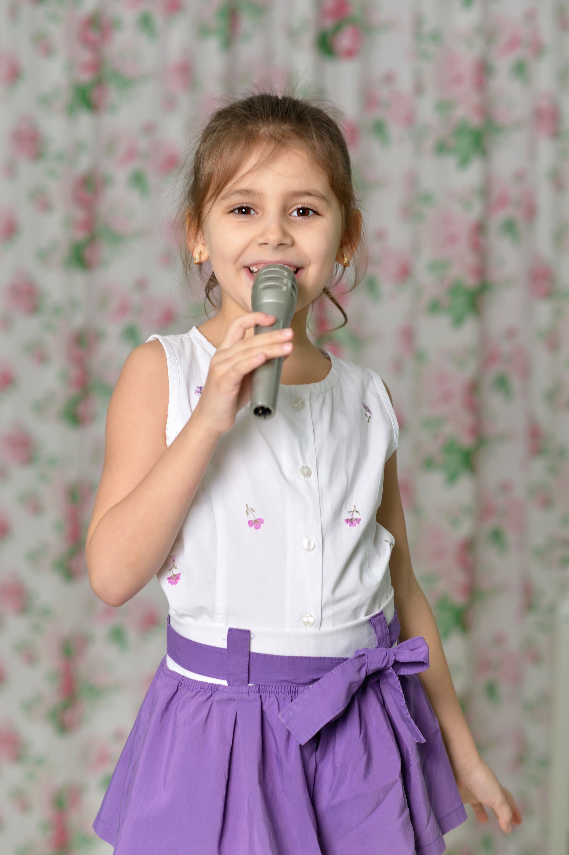A little girl in a purple skirt is singing into a microphone.
