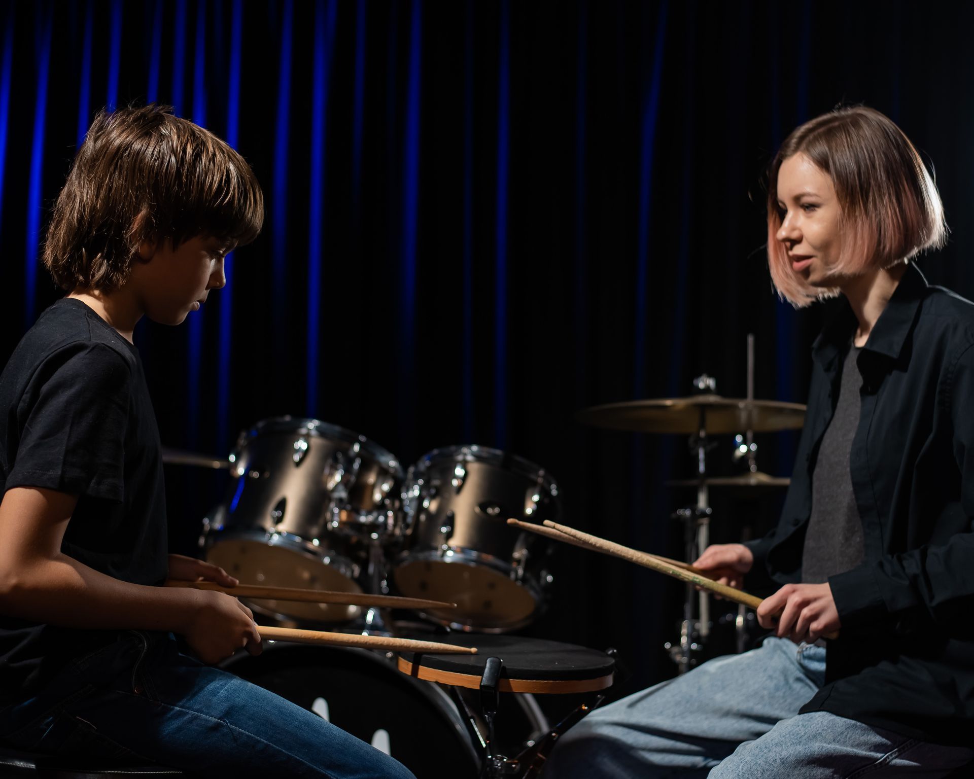 A woman is teaching a young boy how to play drums.